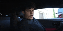 a young man is sitting in a car with a red seat
