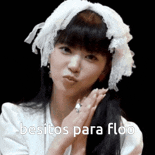 a woman wearing a white headband and a white shirt is sending a kiss with the words besitos para floo below her .