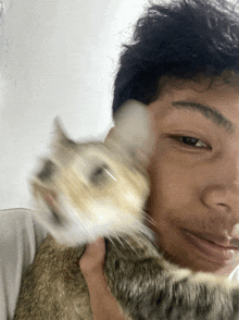 a young man is holding a cat in his arms and the cat is looking at the camera