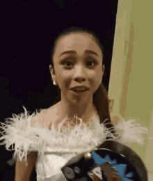 a woman in a white dress with feathers on the sleeves is standing in a dark room .