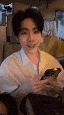 a young man in a white shirt is sitting in a car holding a cell phone .