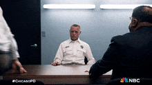 a chicago police officer sits at a desk talking to a man