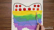 a person is painting a rainbow with cherry tomatoes and the words made in animatica below it