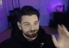 a man with a beard is waving his hand in front of a camera in a room .