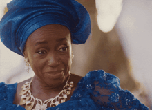 a woman wearing a blue turban and a blue dress looks at the camera