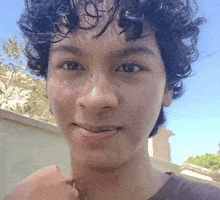 a young man with curly hair looks at the camera with a smile on his face