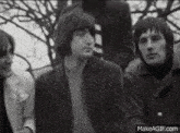 a black and white photo of a group of men standing next to each other in front of a tree .