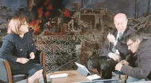 two men and a woman sit at a table with a laptop