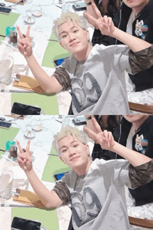 a man with blonde hair giving a peace sign while sitting at a table