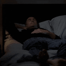 a man in a black shirt is laying in a bed