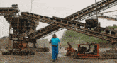 a man in a blue shirt is standing in front of a conveyor belt that says ' t ' on it