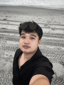 a man wearing sunglasses and a black shirt takes a selfie on the beach