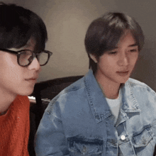 two young men wearing glasses and a denim jacket are sitting next to each other
