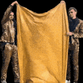 two men in gold suits are holding a yellow cloth