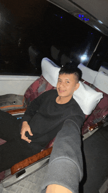 a man in a black shirt sits in a chair with white pillows