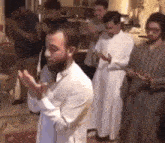 a group of men are standing in a row praying together in a room .