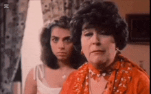 two women are standing next to each other in a room and one of them is wearing a red dress .