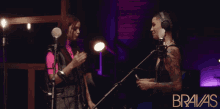 two women singing into microphones with the word bravas on the bottom right