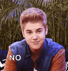 justin bieber is sitting on a couch and smiling while wearing a denim vest and a leather jacket .
