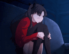 a girl in a red jacket sits on a couch in the dark