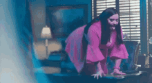 a woman in a pink dress is kneeling on a desk in a living room .
