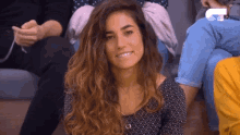 a woman with curly hair is smiling while sitting on the floor in front of a group of people