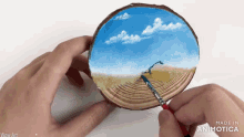 a person is holding a piece of wood with a painting of a landscape on it