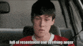 a young man in a red shirt is driving a car with the words full of resentment and seething anger below him