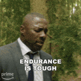 a man in a suit and tie is standing in the woods and says endurance is tough