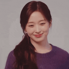 a woman wearing a purple sweater and a ponytail is smiling and looking at the camera .