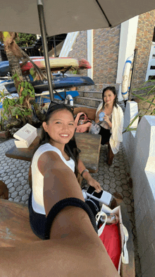 two girls are sitting under an umbrella and one of them is wearing a white tank top that says ' lg ' on it