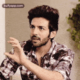 a man with a beard and a plaid shirt is sitting at a table with his hands outstretched .
