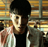 a man with blood on his shirt looks at the camera with a surprised look on his face