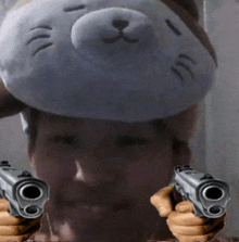 a man with a stuffed animal on his head holds two guns