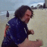 a man in a blue shirt is standing on a sandy beach .