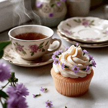 a cup of tea sits next to a cupcake with purple flowers on it