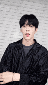 a young man wearing a black jacket and a bracelet looks at the camera