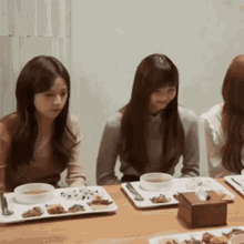 a group of young women are sitting at a table with plates of food and bowls of soup .