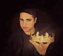a young man is holding a gold crown in his right hand
