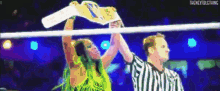 a woman in a green dress is holding a wrestling championship belt over a referee 's head .
