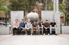 a group of men are sitting on a bench with one wearing a black shirt that says ' a.p.m. '