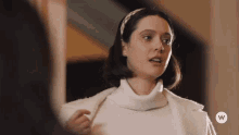 a woman wearing a white sweater and a white coat with a w on the bottom right