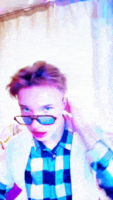 a boy wearing sunglasses and a plaid shirt adjusts his ear