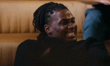 a man with dreadlocks is sitting on a couch laughing