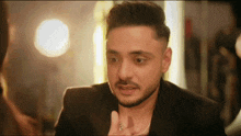 a man with a beard is wearing a black jacket and a silver necklace