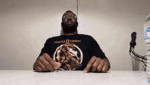a man wearing a mortal kombat shirt sits at a table next to a bottle of aquafina water