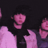 a group of people are standing next to each other in a dark room . one of the people is wearing a purple jacket .