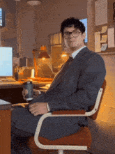 a man in a suit and tie sits in an office chair holding a cup of coffee
