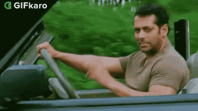 a man is driving a car down a road and holding the steering wheel .