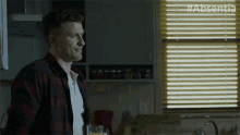 a man in a plaid shirt stands in front of a window with #absentia written on the bottom
